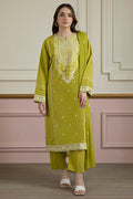 Woman wearing a green embroidered traditional outfit against a decorative wall.