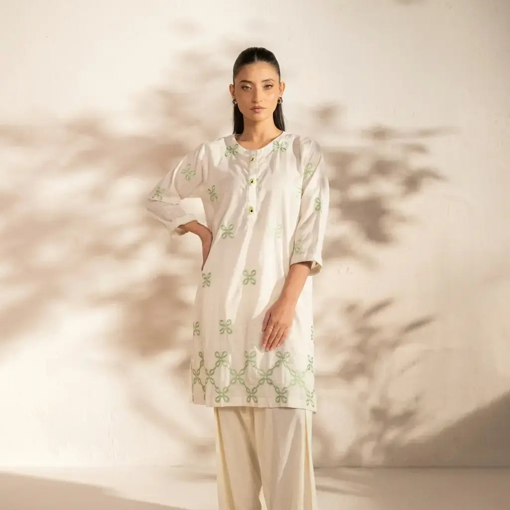 Woman wearing a white embroidered kurta with green patterns against a neutral background